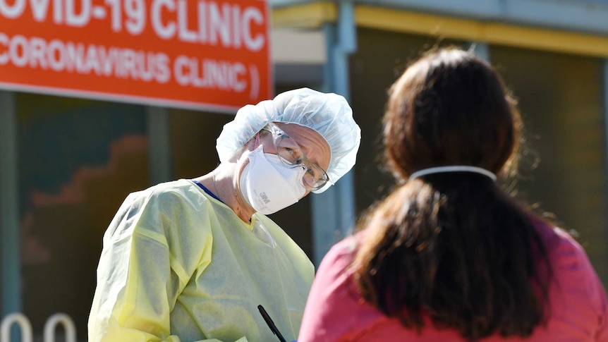 A doctor in protective gear talks to a woman outside a coronavirus testing clinic