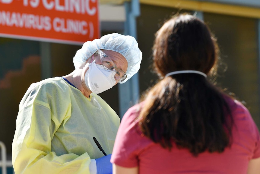 A doctor in protective gear talks to a woman outside a coronavirus testing clinic