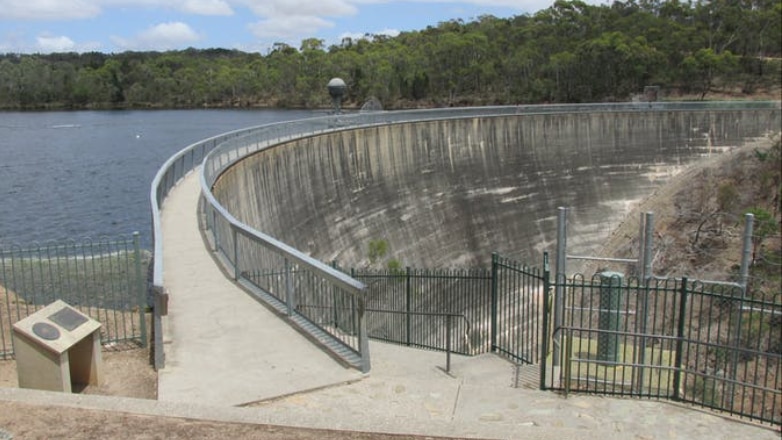 A large concrete dam wall with water on one side stretches into the distance