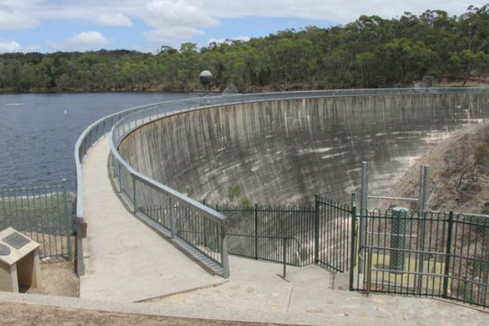 A large concrete dam wall with water on one side stretches into the distance
