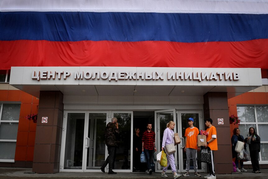 People carry goods as they walk out of the shelter in Belgorod draped the Russian flag