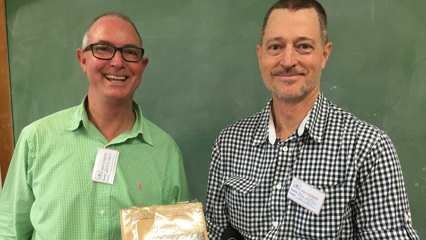 Two men hold a book detailing corporal punishment in the school.