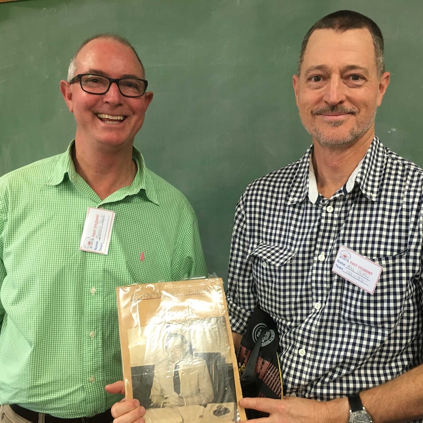 Two men hold a book detailing corporal punishment in the school.