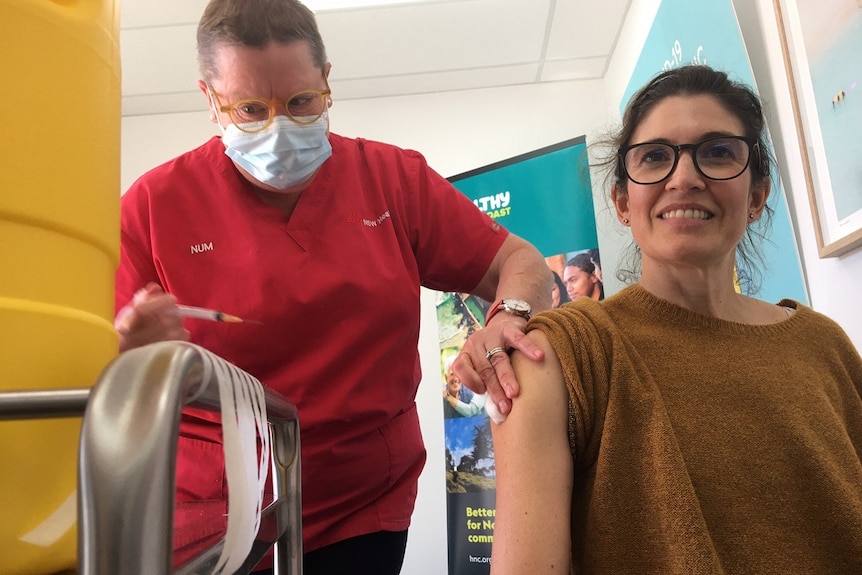 A dark-haired woman wearing dark-rimmed glasses and a brown jumper receives her second dose of AstraZeneca vaccine