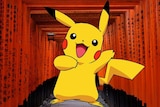 Pokémon mascot Pikachu, a yellow cartoon, inside a red Shinto walkway with Japanese letters printed on wooden posts.