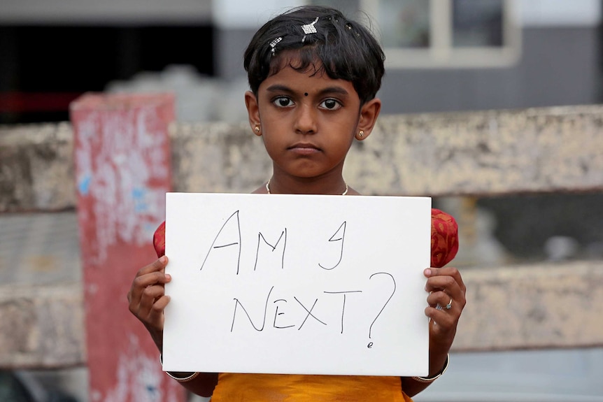 A young girl holding a sign reading "Am I next?"