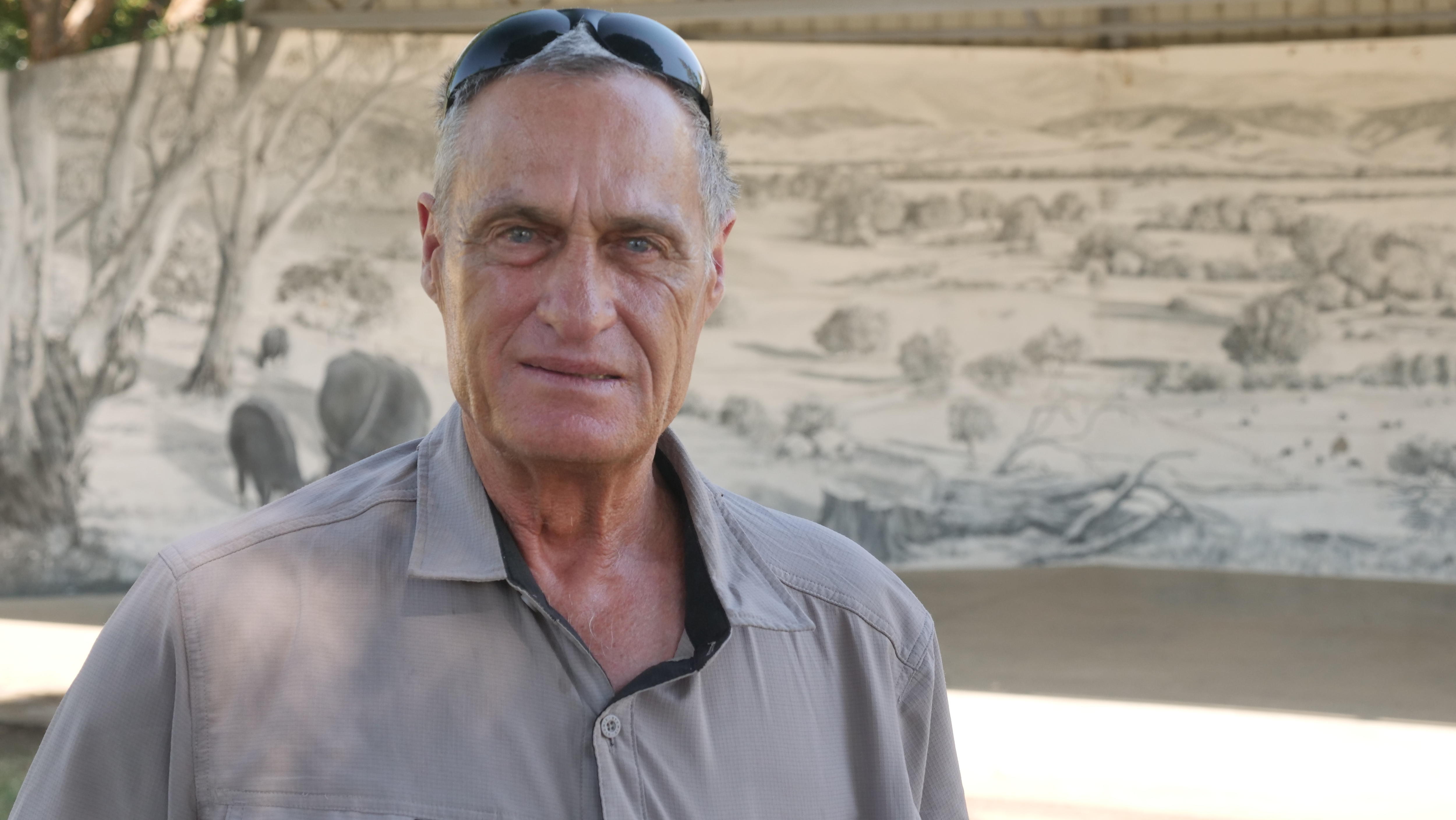 A man looks at the camera with a mural behind him. 