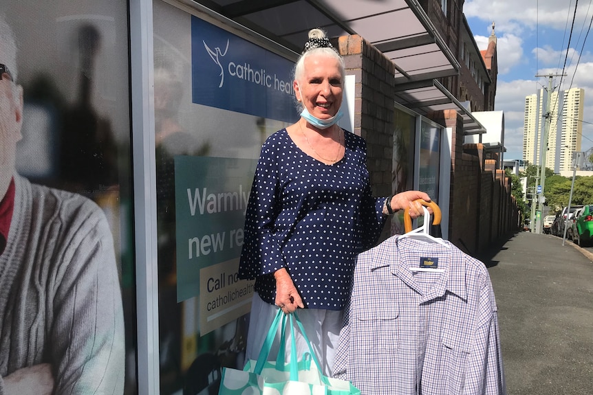 Mary Shang Loftus stands in a street holding ironed shirts and a green bag.