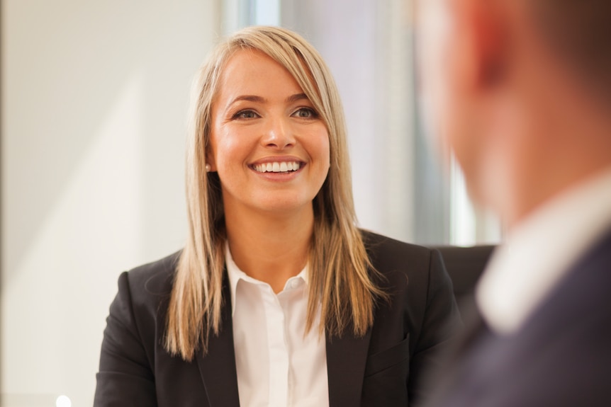 A blonde woman in corporate attire smiling