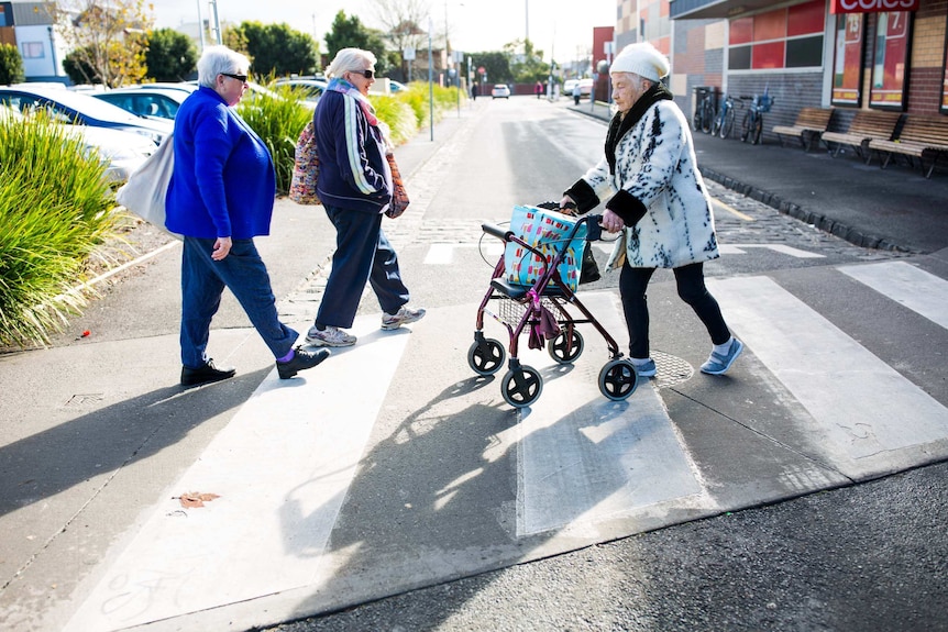 Bev Howlett crossing a road at a crosswalk with her walker.