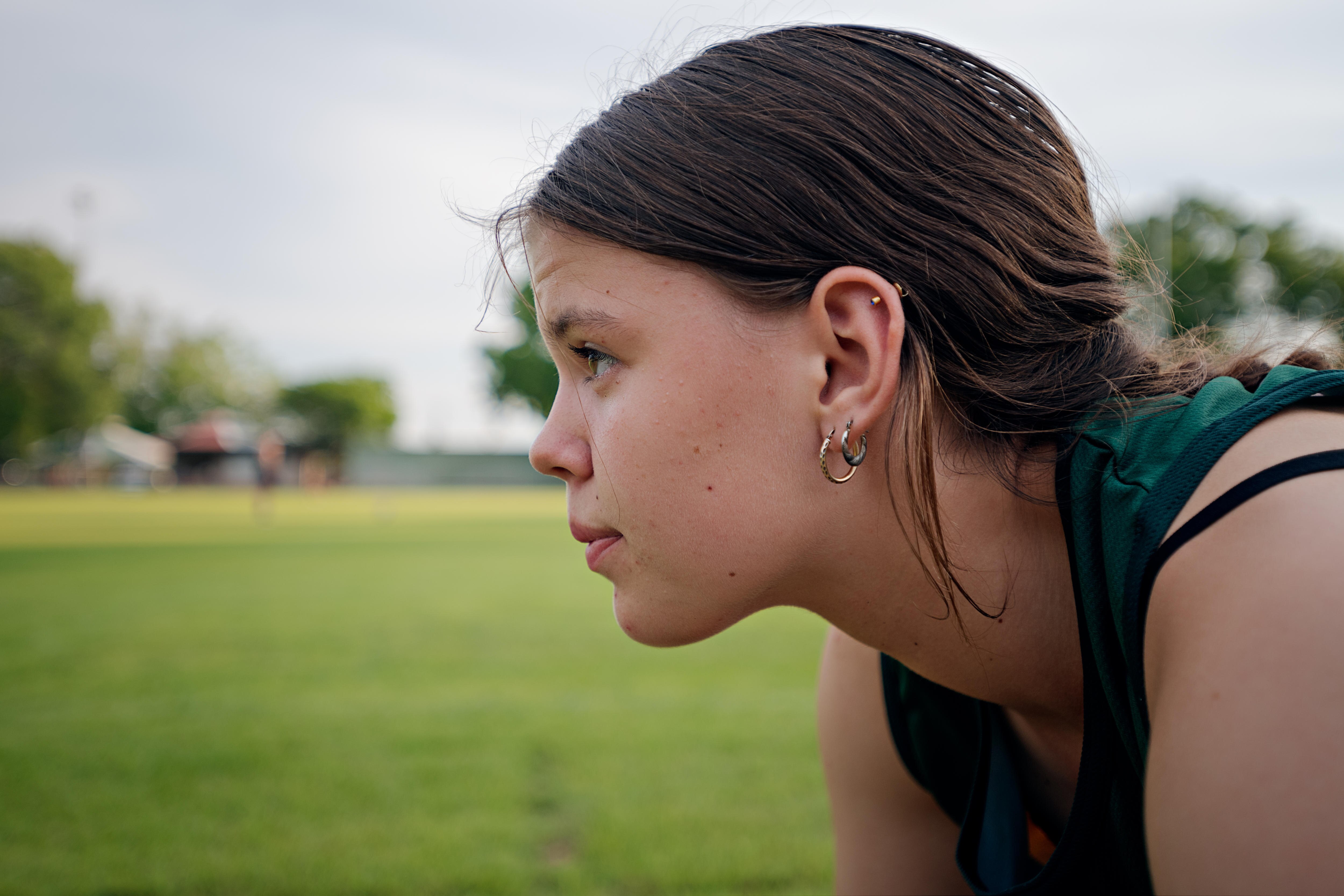 A close-up side profile of a teenage girl who bends forward in preparation for a sprint