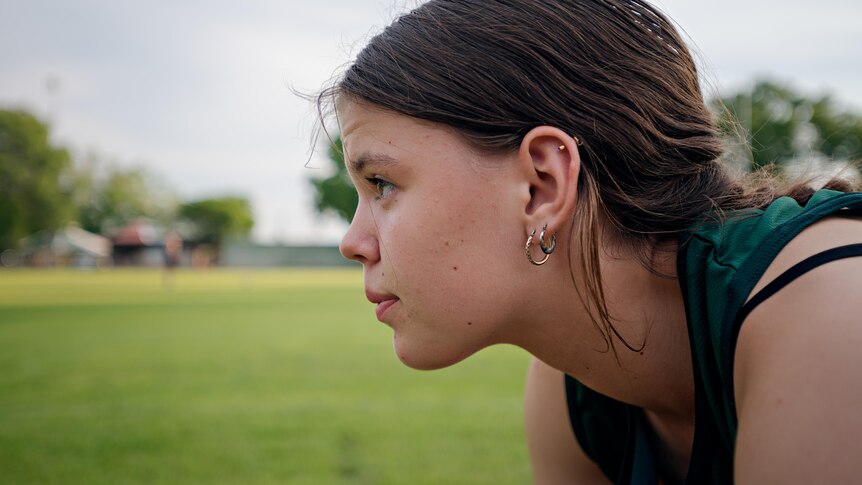 A close-up side profile of a teenage girl who bends forward in preparation for a sprint