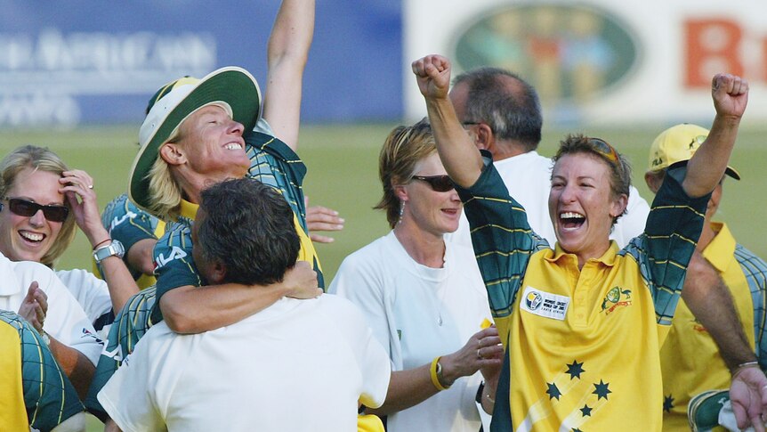 One woman Australian cricketer embraces someone, while another has her arms in the air in celebration.
