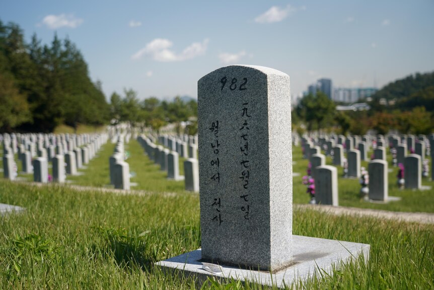 An engraved gravestone surrounded by other grey gravestones in a field of green grass.
