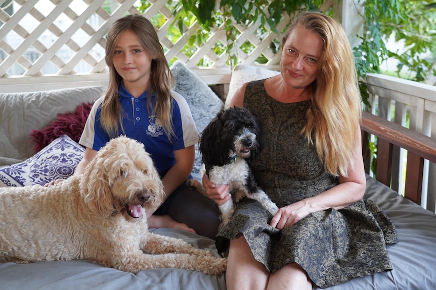 A woman and a child sit outside with two dogs.