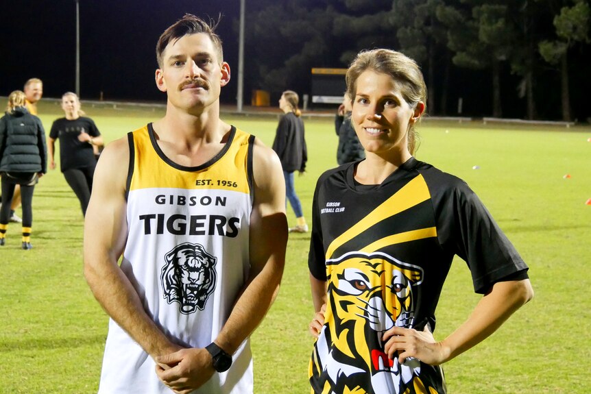 A man and a woman stand side by side on a football oval. 