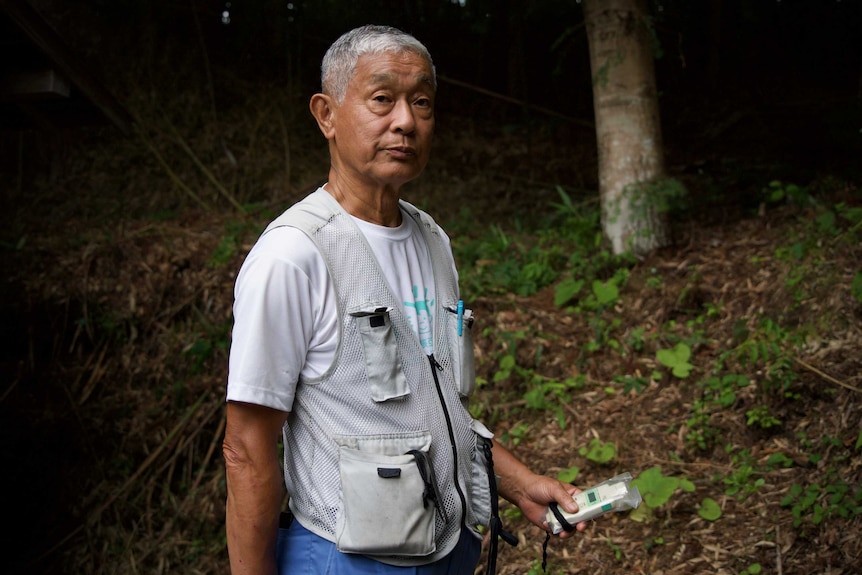 An older Japanese man in a vest holds a radiation reader
