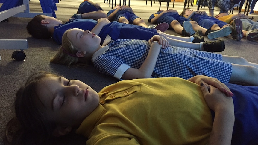 Students lie on the floor with their eyes closed
