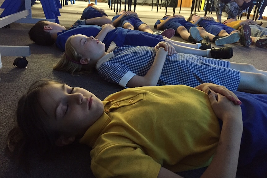 Students lie on the floor with their eyes closed