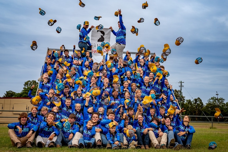 Camp participants wearing blue shirts on a grandstand, throwing their caps in the air.