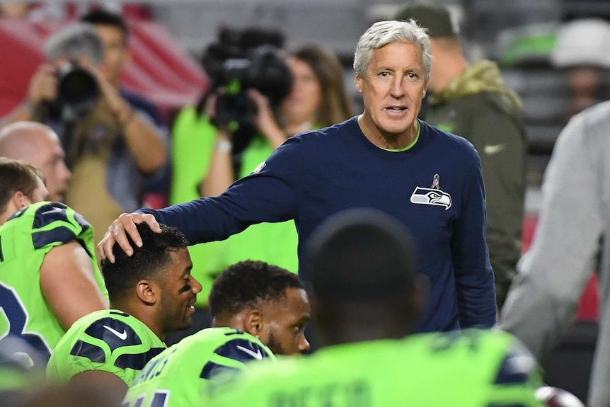 Medium telephoto shot of a coach with his hand on a kneeling football player's head.