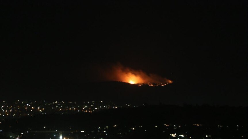 View form a hill overlooking Canberra at night, with blazes burning on hills in distance.