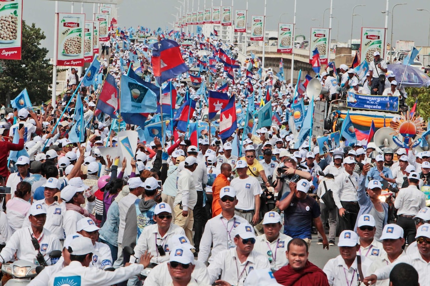 Cientos de simpatizantes del Partido Nacional de Rescate de Camboya con sombreros de fiesta blancos y ondeando banderas en un mitin preelectoral.