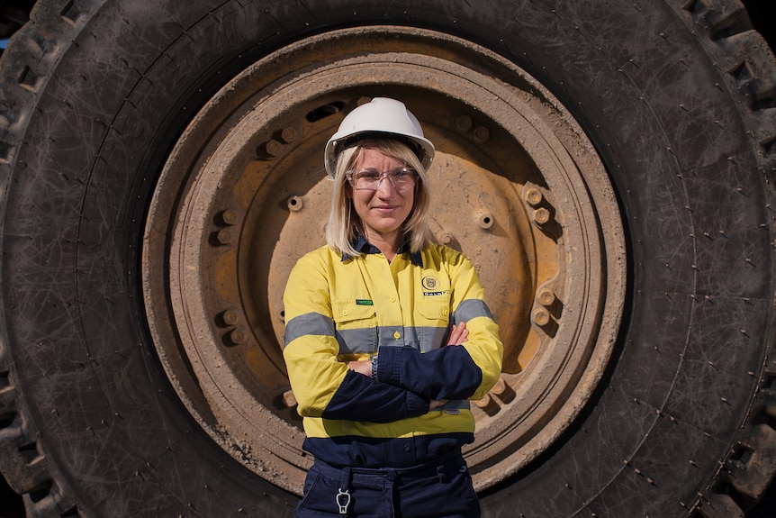 A woman with a hard hat and high-vis clothes stands in front of a giant tyre.