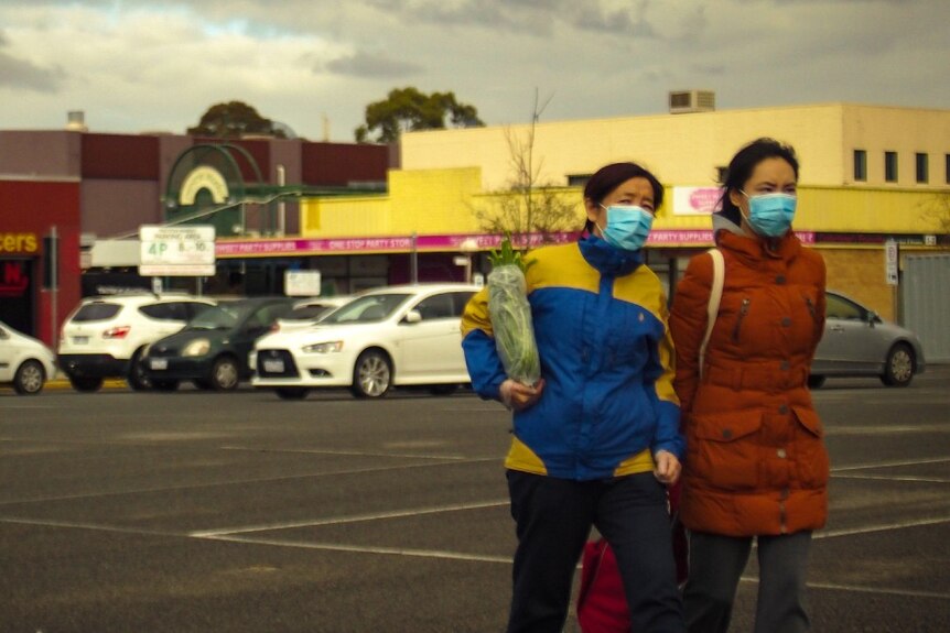 Two women wearing blue surgical masks and carrying shopping walk across a carpark in Preston.