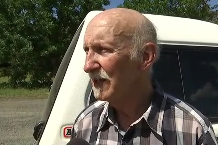 Doug Maclean stands on a road in front of his car.