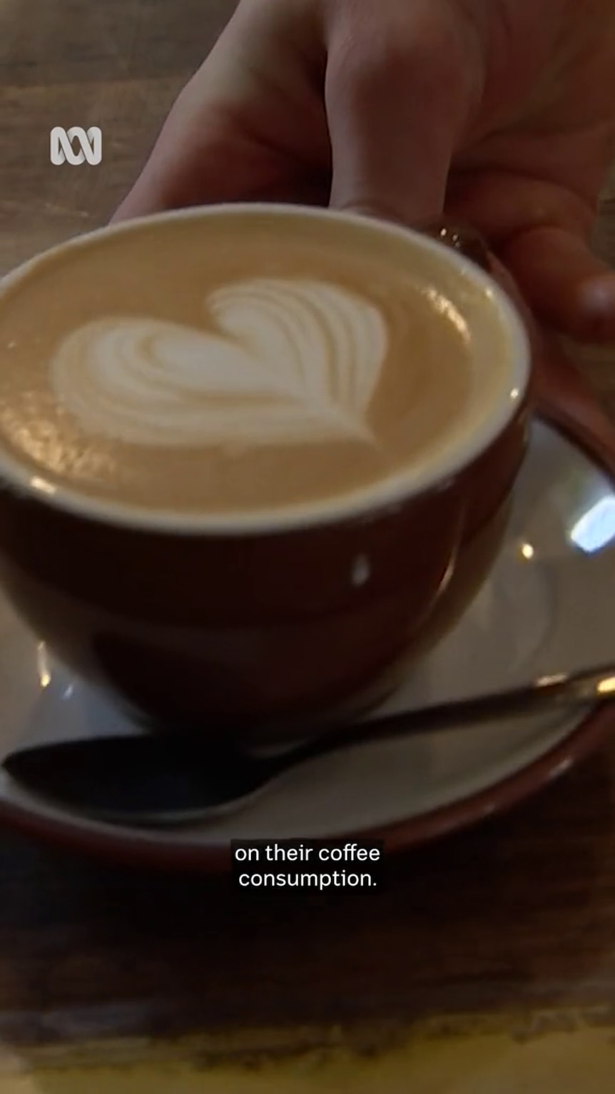 Latte art is displayed inside a dark coffee cup