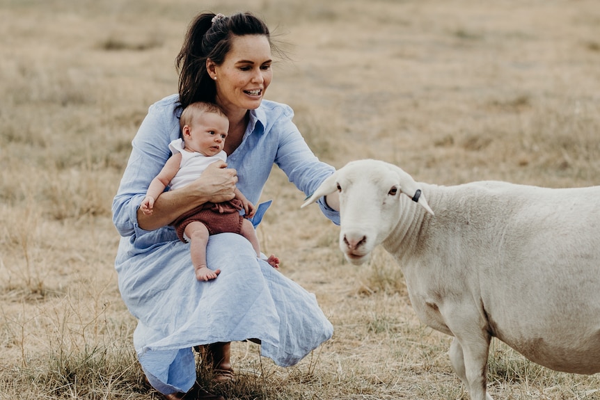 Lady pets a lamb with baby perched on knee