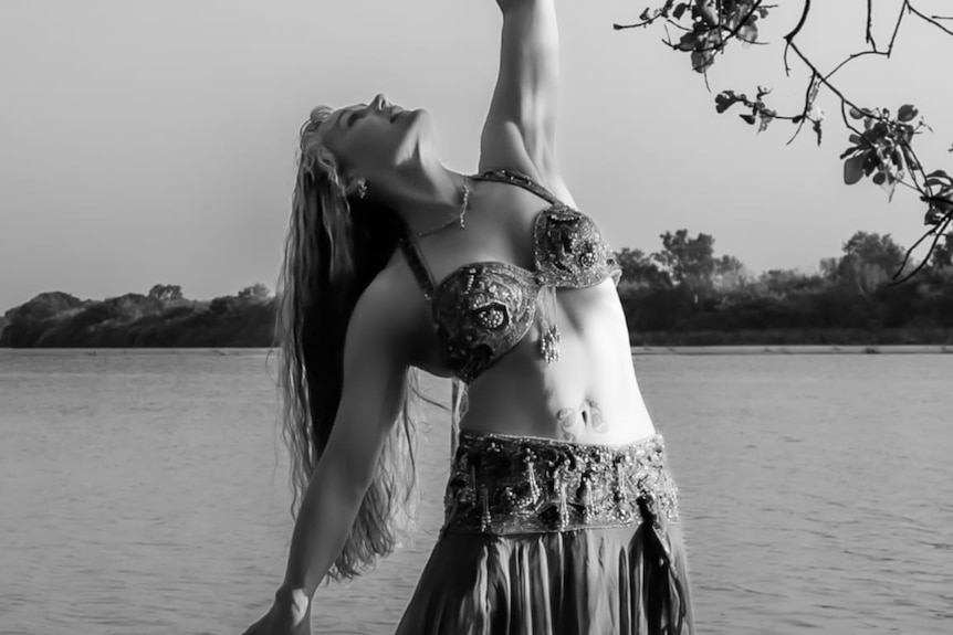 A woman in a belly dancing outfit poses with arms uplifted