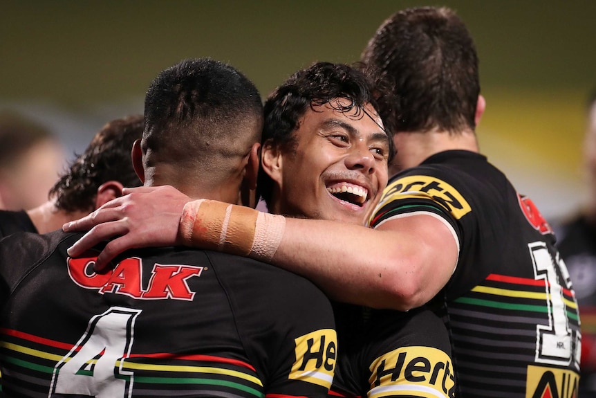 A Penrith NRL player smiles as he hugs Panthers teammates while they celebrate a try against the Rabbitohs.