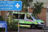 An ambulance parked outside Royal Perth Hospital with a blue sign for the emergency department in the foreground.