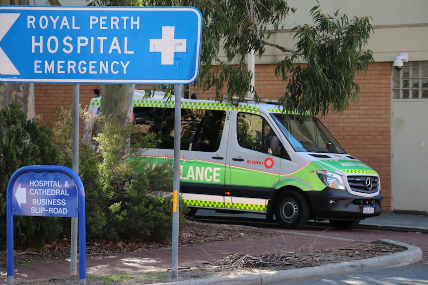 An ambulance parked outside Royal Perth Hospital with a blue sign for the emergency department in the foreground.