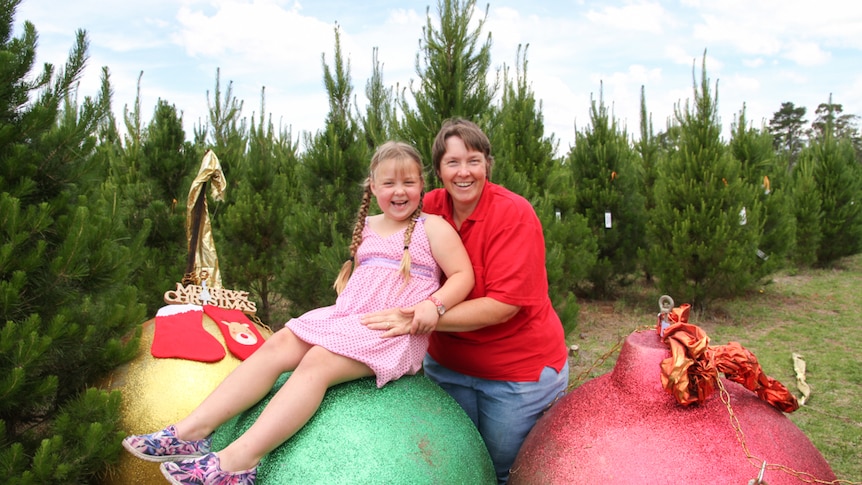 Woman holds child on a giant Christmas bauble in a Christmas tree paddock