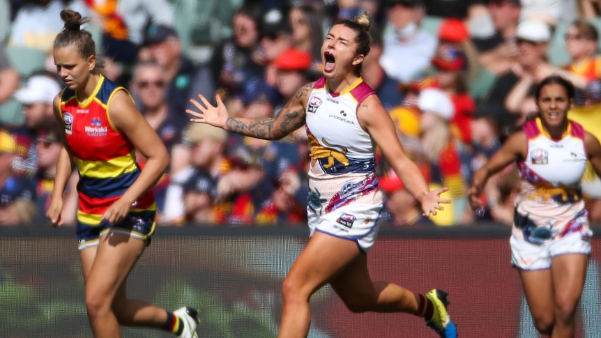 A cheering Brisbane player runs with her arms outstretched. 