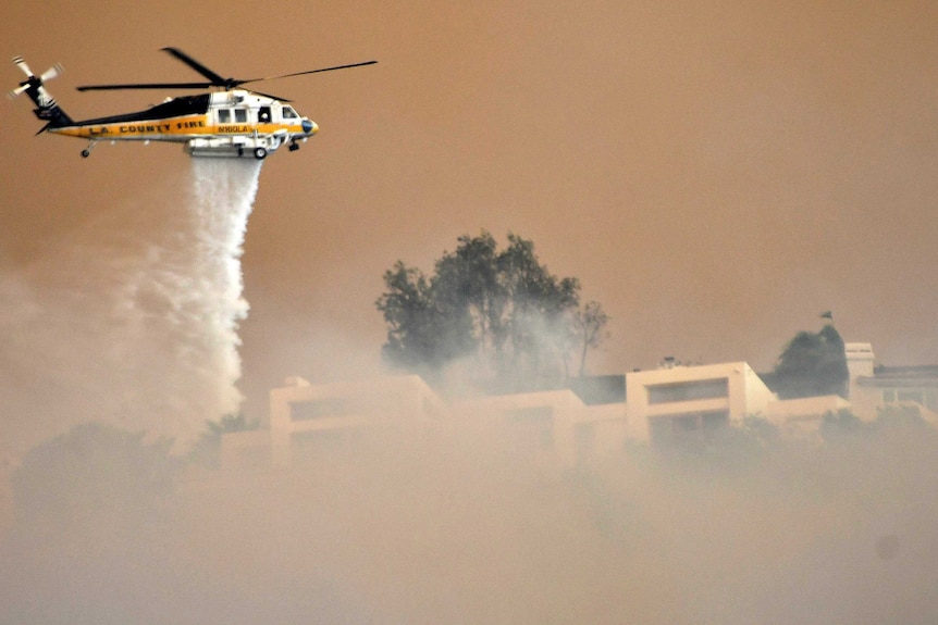 A helicopter drops water through thick smoke onto a building.
