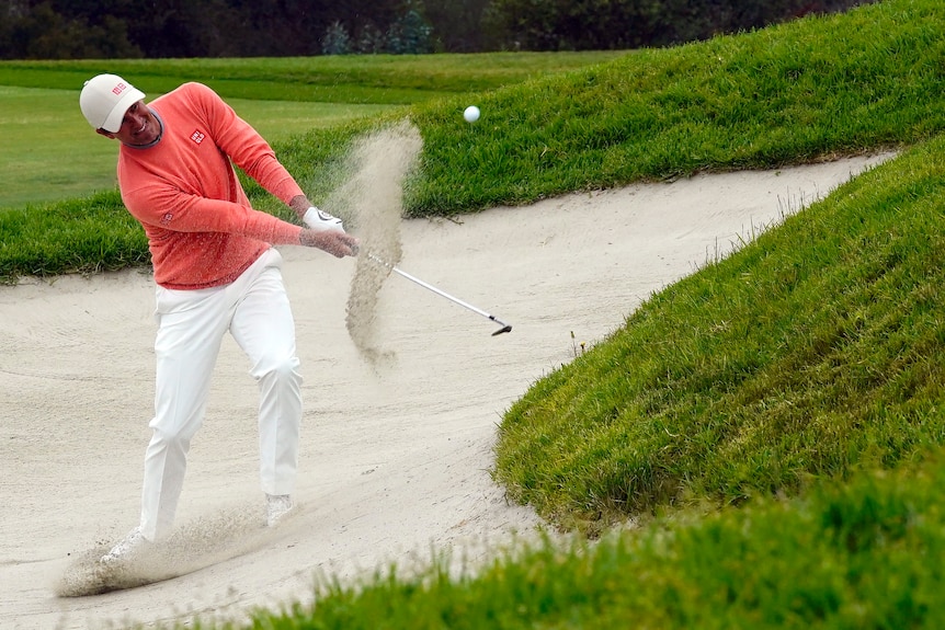 A spray of sand flies up as an Australian golfer chips out of a bunker at the US Open.