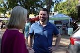 A woman and man speaking on the outskirts of an outdoor market, on a sunny day.