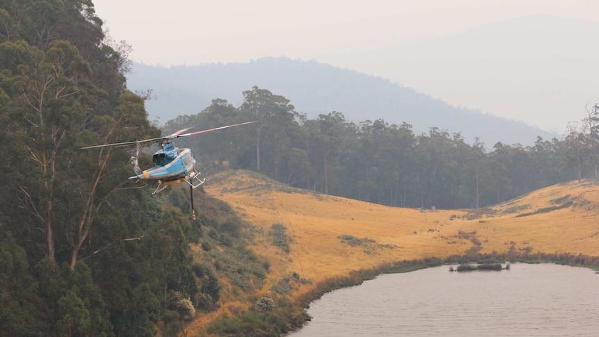 A waterbombing helicopter approaches a dam near Glen Huon