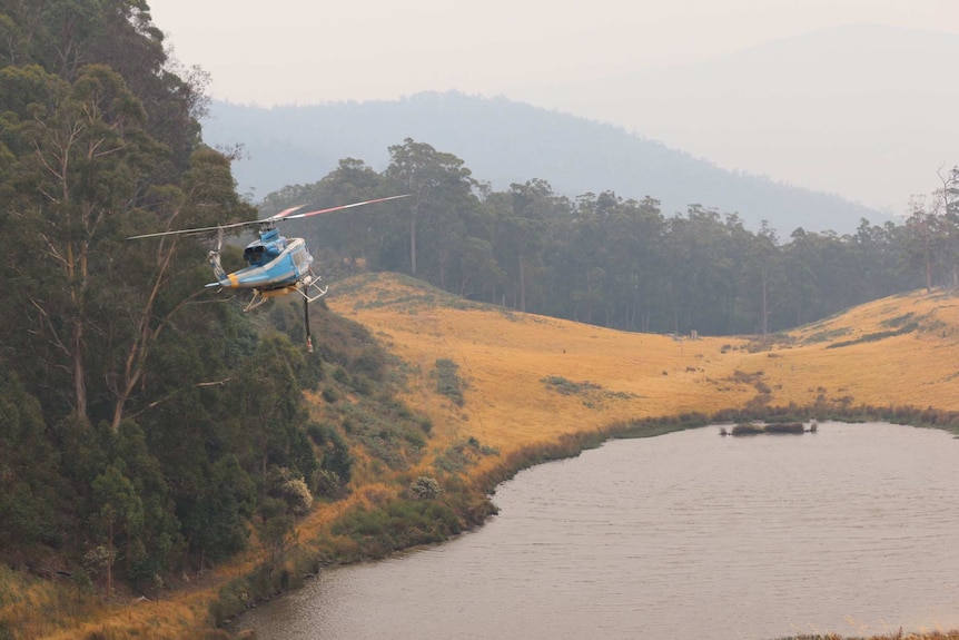 A waterbombing helicopter approaches a dam near Glen Huon