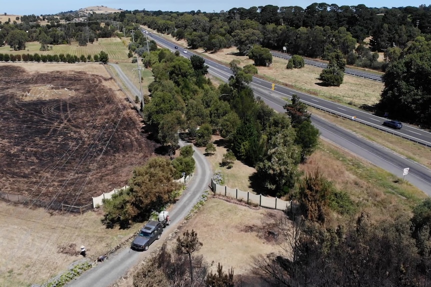 A birds-eye view from a drone of burnt paddock one one side of a road and a property on the other.