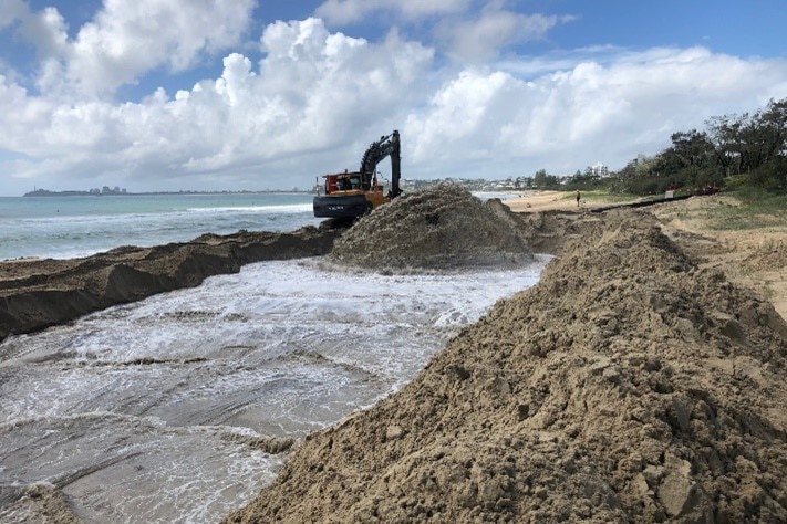 An excavator and large piles of sand on the beach.