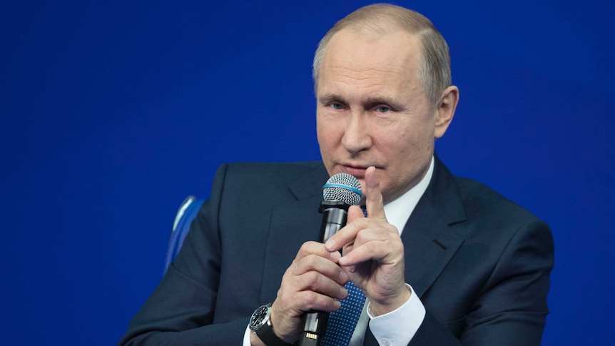 Russian President Vladimir Putin holds a microphone.