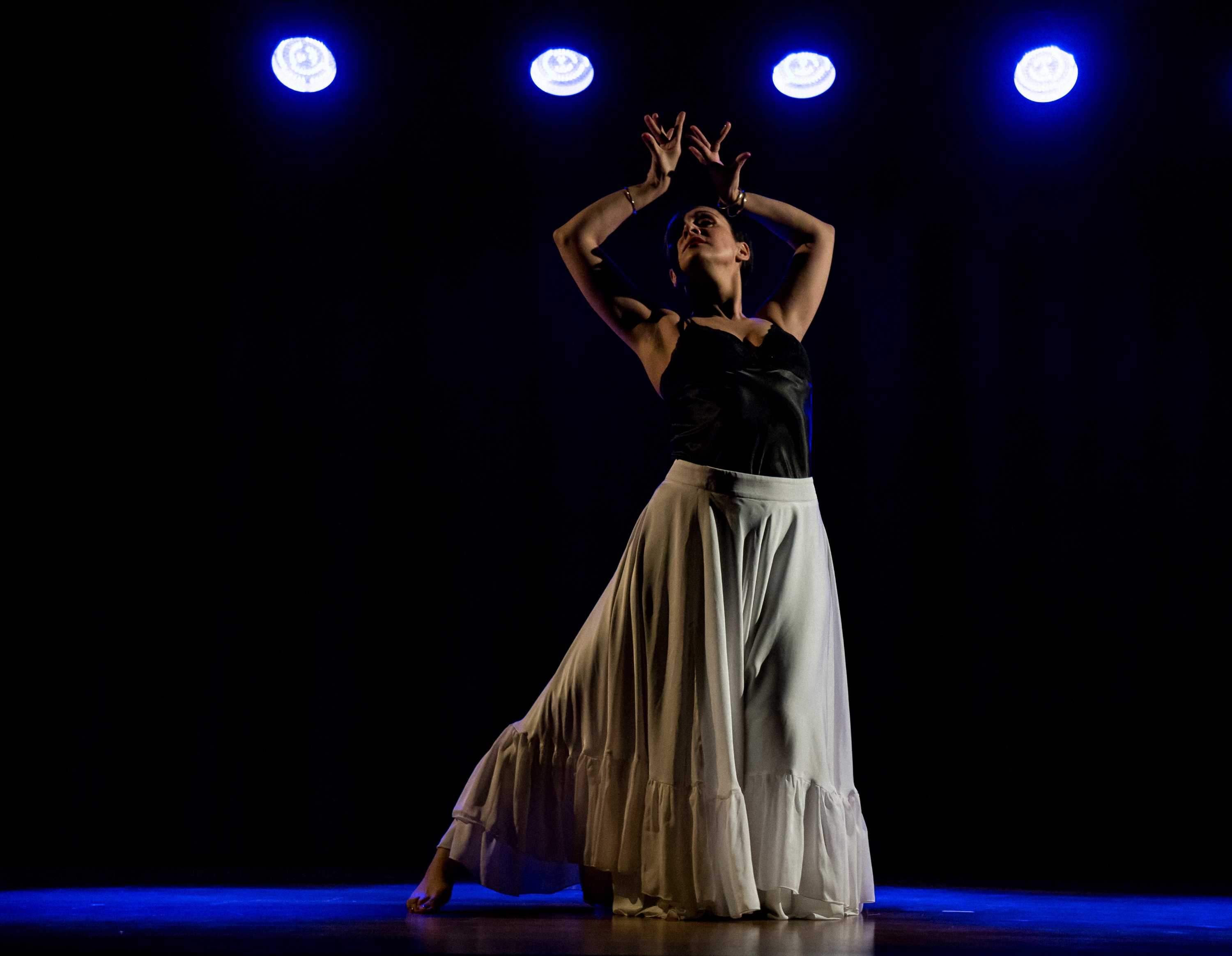 A women holds her hands above her head as she dances below a row of blue lights.