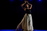 A women holds her hands above her head as she dances below a row of blue lights.