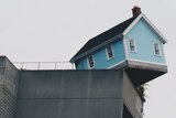 shot of blue weatherboard house teetering on the edge of a building