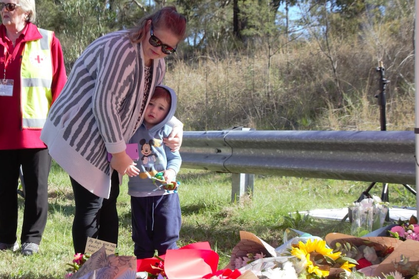 Woman and young child look at a pile of floral tributes lid at the site of the Hunter Valley bus crash